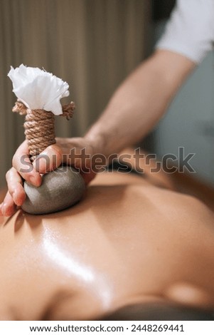 Cropped vertical shot of Ayurveda Massage therapist pressing herbal bolus bags onto female skin. Masseur gently compresses herb bag on woman body. Hot herbal ball spa massage body treatment. Royalty-Free Stock Photo #2448269441