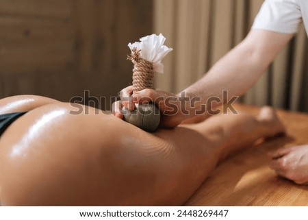 Closeup of Herbal Ayurvedic massage with Kizhi Herbal Bags on buttocks. Relaxed female client receiving herbal bolus bags massage. Tranquil and serenity of aromatherapy recreation at spa salon. Royalty-Free Stock Photo #2448269447