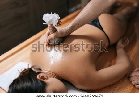 High-angle view of relaxed young woman lying with closed eyes receiving herbal bolus bags massage. Closeup hands of Ayurveda massage therapist pressing herbal bolus bags onto female body. Royalty-Free Stock Photo #2448269471