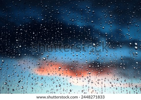 Stunning photoshoot of raindrops on a window with background of sunset in the sky. Wallpaper image with water drops and blurred sky and clouds on the background