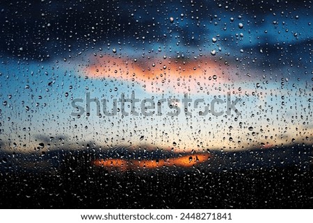 Stunning photoshoot of raindrops on a window with background of sunset in the sky. Wallpaper image with water drops and blurred sky and clouds on the background