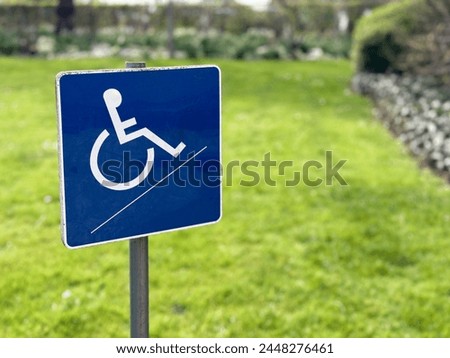 A small blue wheelchair handicap sign stands against a blurred garden background, symbolizing accessibility and inclusivity in outdoor spaces.