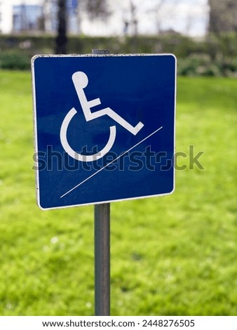 A small blue wheelchair handicap sign stands against a blurred garden background, symbolizing accessibility and inclusivity in outdoor spaces.