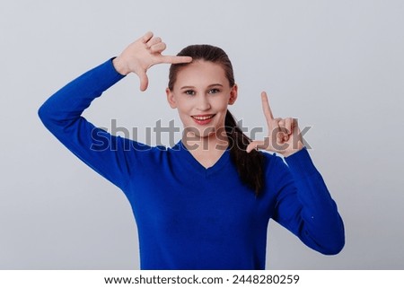 young caucasian beautiful woman in blue sweatshirt showing photo frame gesture with fingers and smiling