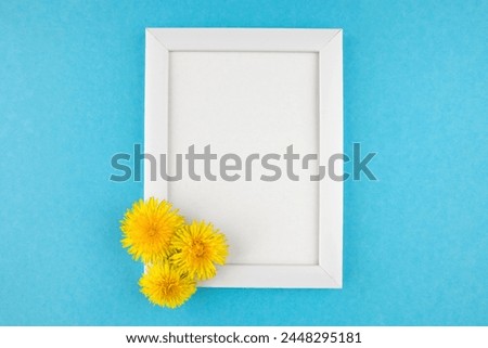 White wooden photo frame and flowers on blue background with copy space.