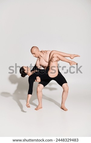 Shirtless young man and dancing young woman perform acrobatic pose in perfect harmony against a white backdrop.