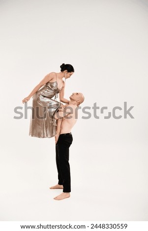 A shirtless young man and a woman in a shiny dress dance performing acrobatic elements. Studio shot on a white background.