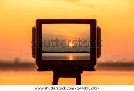 Silhouette of TV frame on bench with beautiful sunset at the lake.