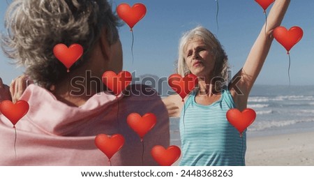 Image of red heart balloons, over women exercising on beach. positive feelings and wellbeing social media concept, digitally generated image.