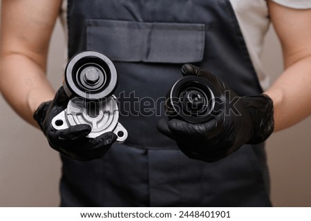 Auto mechanic holds in hands in black gloves tension roller with car serpentine belt tensioner and parasitic roller, close-up. Replacing auto parts, car maintenance, purchasing auto parts Royalty-Free Stock Photo #2448401901