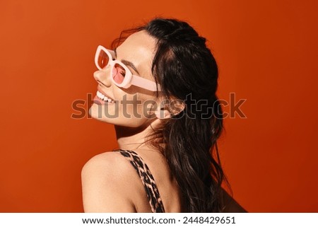 A fashionable woman exudes confidence in pink sunglasses and a leopard print dress against a vibrant orange backdrop.