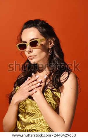 A stylish woman exudes summer vibes in a vibrant yellow dress and chic sunglasses against an orange studio backdrop.