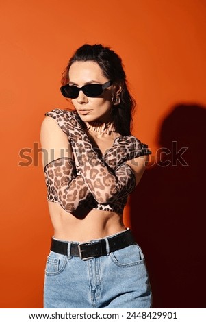 A fashionable woman poses in leopard print top and sunglasses on an orange background, exuding summertime chic.
