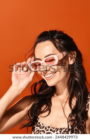 A stylish woman exudes confidence in pink sunglasses and a leopard print top against an orange background.