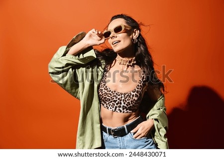 A stylish woman wearing a leopard print top and jeans, exuding confidence and summertime fashion on an orange studio background.