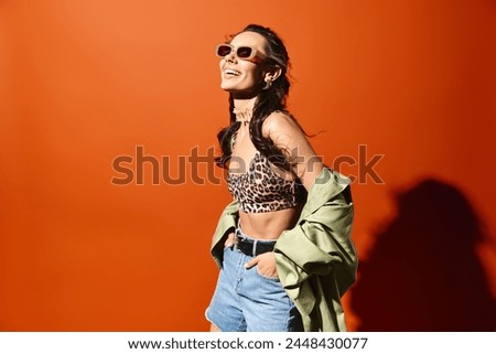 A fashionable woman wearing a leopard print top and denim shorts, exuding confidence and style on an orange background.