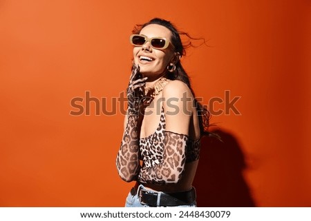 A stylish woman rocks a leopard print top and sunglasses, exuding summertime charm against an orange background.