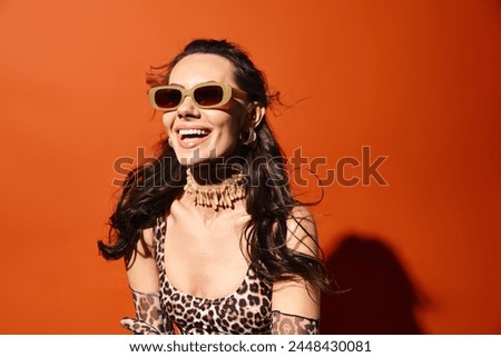 A fashionable woman exudes confidence in a leopard print dress and chic sunglasses against an orange studio backdrop.