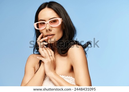 A stylish woman donning pink sunglasses strikes a pose for a portrait in a studio against a vibrant blue backdrop.