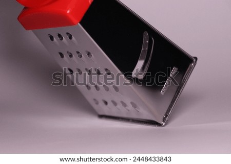 a small vegetable grater with a red handle on a white background