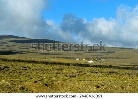 Photography of a placid landscape, a farm, a field, a slope and a sky with fluffy clouds
