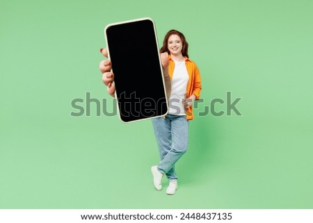 Full body young ginger woman wear orange shirt white t-shirt casual clothes hold in hand use mobile cell phone with blank screen workspace area isolated on plain green background. Lifestyle concept