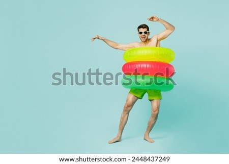Full body young man wear green shorts swimsuit glasses relax near hotel pool in three inflatable rings dance raise up hands isolated on plain blue background. Summer vacation sea rest sun tan concept Royalty-Free Stock Photo #2448437249