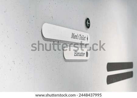 Gray concrete wall with directional signs indicating men's toilet and elevator