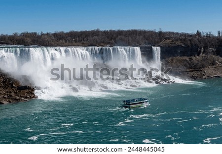 A Tourist Boat Carrying People Passing Niagara Falls USA and Heading Towards Niagara Falls Canada on a Sunny Spring Day Royalty-Free Stock Photo #2448445045