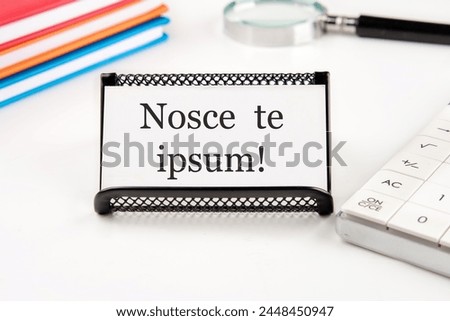 Latin proverb NOSCE TE IPSUM (know yourself) on a white business card on a table with office supplies