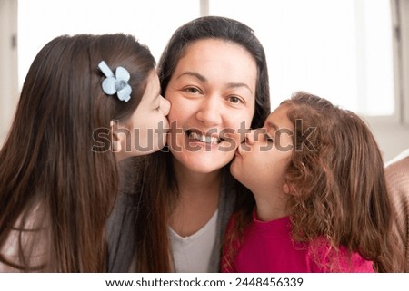 Joyful brazilian mother and daughters kissing in the cheek. at family home. Unity, happiness, affection, love, care concept.