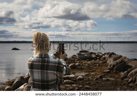 A girl takes a photo on her phone on the seashore of the Baltic Sea during the day. 