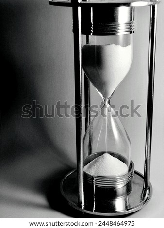Black and white photograph of white sand falling in sand timer making shadow on white background