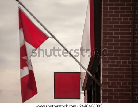 Selective blur on An empty red signboard of a retail shop poised for branding, with the Canadian flag waiving above, with a backdrop of a traditional brick wall, signifying business  national identit