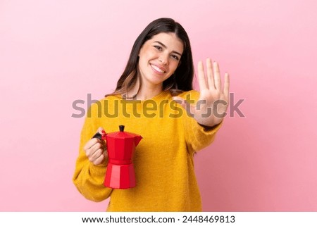 Young Italian woman holding a coffee maker isolated on pink background counting five with fingers
