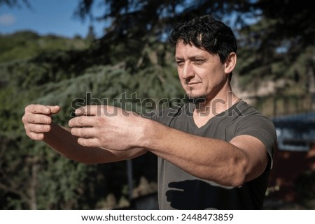 A Caucasian man adopts the Tree Hugging Posture during his Qi Gong training session. Rooted in ancient Chinese practices, this posture cultivates internal strength, balance, and energetic alignment. Royalty-Free Stock Photo #2448473859