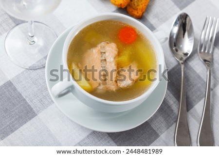 Appetizing rich salmon backbone soup with potatoes and carrots served in white tureen with crispy toasts .. Royalty-Free Stock Photo #2448481989