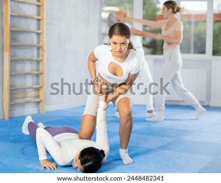 Concentrated young woman practicing armlock, painful control move to hold and immobilize opponent, in training bout during self defence course in gym .. Royalty-Free Stock Photo #2448482341