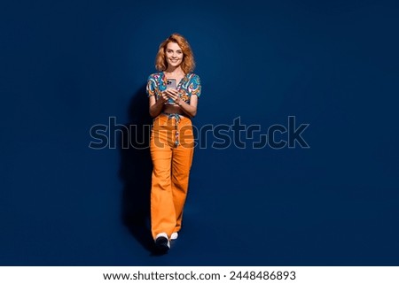 Full size photo of pretty young woman texting smart phone walk empty space wear top isolated on dark blue color background
