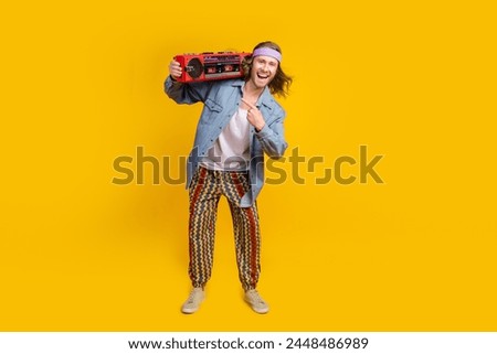 Full body portrait of cool young man direct finger boombox empty space wear denim shirt isolated on yellow color background