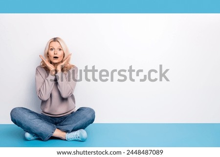 Full body photo of senior lady sit floor crossed legs empty space afraid dressed stylish gray garment isolated on blue color background