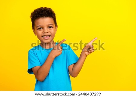 Photo of small child with curly hair dressed blue t-shirt indicating at proposition empty space isolated on vibrant yellow background