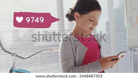 Close up of a little girl leaning on a bike near the window while texting on her phone. Beside her is a digital image of a message bubble with a heart icon increasing in count