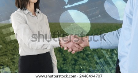 Close up of a handshake between a man and a woman wearing corporate attire with a background of a wide field filled with trees. Digital image of graphs and statistics are running in the foreground.