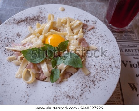 creamy white source pasta with bacons, green herb and raw egg on the table of cafe in ukraine