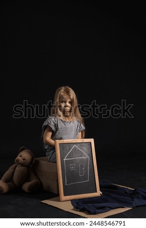 Homeless little girl with picture of house and teddy bear on dark background