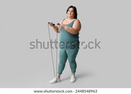 Happy young overweight woman with jumping rope on grey background. Weight loss concept