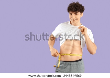 Handsome young happy sporty man with measuring tape on purple background. Weight loss concept
