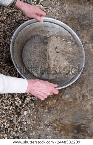 Searching for gold with an iron pan in a riverbed. Gold panning Royalty-Free Stock Photo #2448582209