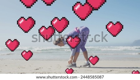 Image of floating red pixel hearts, over woman tying shoe on beach. positive feelings and wellbeing concept, digitally generated image.